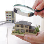 住宅の模型と虫眼鏡を持つ手